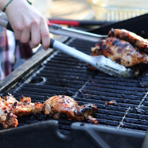 young man in plaid shirt grabbing grilled teriyaki chicken thighs off of a hot grill with tongs